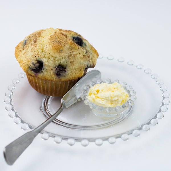 Blueberry muffin made with classic homestyle muffin mix on clear glass plate with knife and small dish of butter.