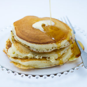 Stack of Buttermilk Pancakes made with buttermilk pancake mix with melting butter and syrup dripping down the stack. Fork sitting next to pancakes on clear glass plate.