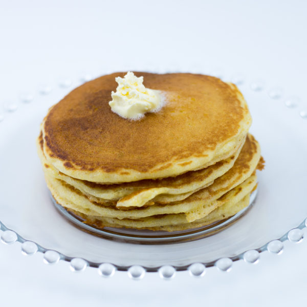 Short stack of cornmeal pancakes made with cornmeal pancake mix with melting butter on top, sitting on clear glass plate.