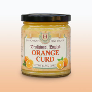 A glass jar with a black cap filled with Orange Curd. The label states it is made by Harrowgate Fine Foods, and is Traditional English Orange curd.