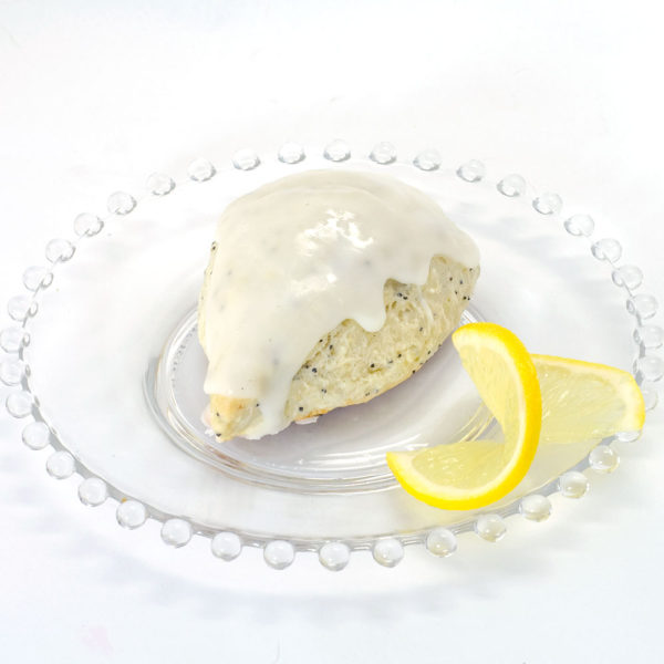 Lemon Poppyseed Scone made with Lemon Poppyseed Scone Mix. The scone is sitting on a clear glass plate, glazed with a lemon glaze, and garnished with a thin slice of fresh lemon.