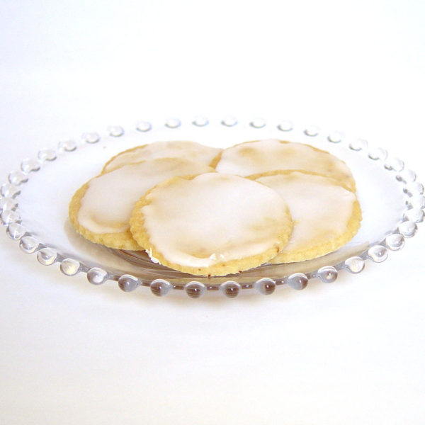 Five round lemon shortbread cookies glazed with a lemon glaze on glass plate