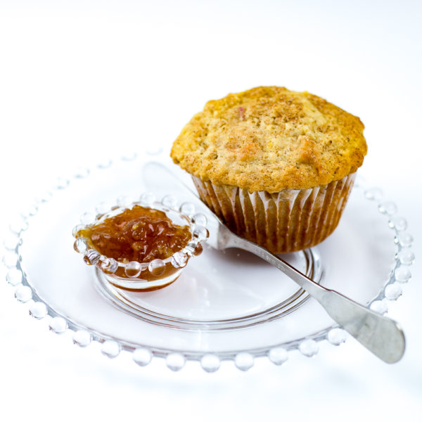 Freshly baked Oatmeal Muffin made with Oatmeal Muffin Mix witting on glass plate with small dish of jam and a spreading knife.