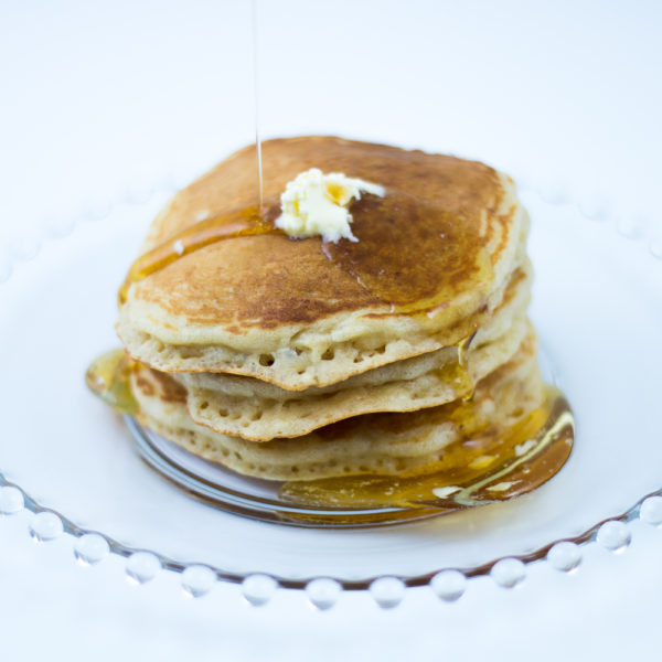 Short stack of Oatmeal Pancakes made with Oatmeal Pancake Mix with melting butter, and syrup being poured on, on glass plate.