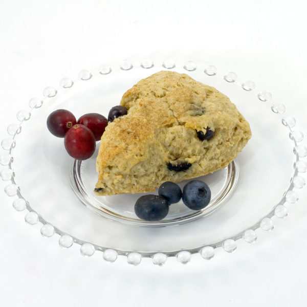 Blueberry-Oatmeal scone made with Original Oatmeal Scone Mix. The scone is sitting on a clear glass plate, and the plate is garnished with blueberries and fresh cranberries.