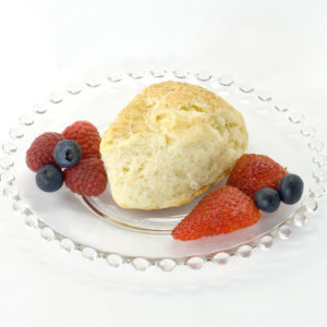 Plain scone made with Original Recipe Scone mix sitting on clear glass plate, garnished with raspberries, strawberries, and blueberries.