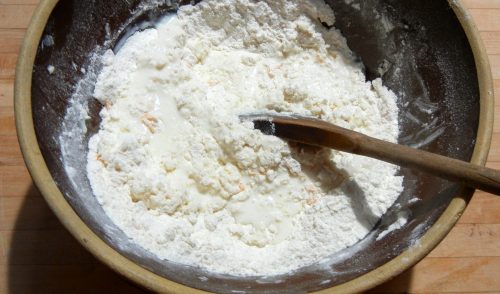 Mixing bowl with flour-butter mixture to which buttermilk has been added. A wooden spoon is used to stir the liquid into the dry ingredients.