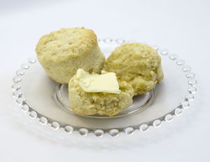 two southern style biscuits on clear glass plate, one cut open and spread with butter