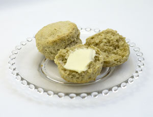 Two oatmeal biscuits on clear glass plate plate with one split open and buttered.