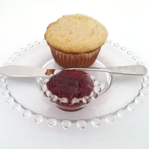Cornmeal muffin made with VHS cornmeal muffin mix on glass plate with preserves in a small glass dish and a knife on the side of the plate
